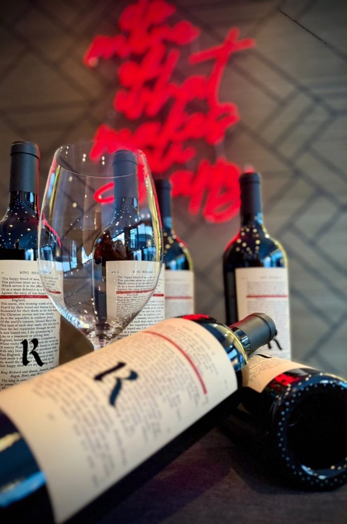 Realm Cellars The Bard, Flaschen und Weinglas vor roter Neonschrift im Christian & Friends Tastekitchen